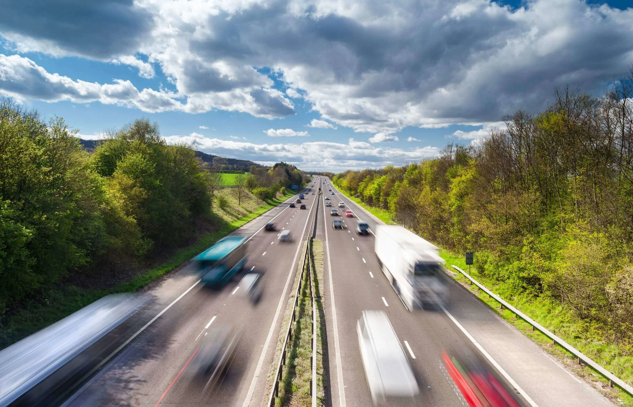 Cars and lorries speeding along a road in both directions with trees and bushes on each side